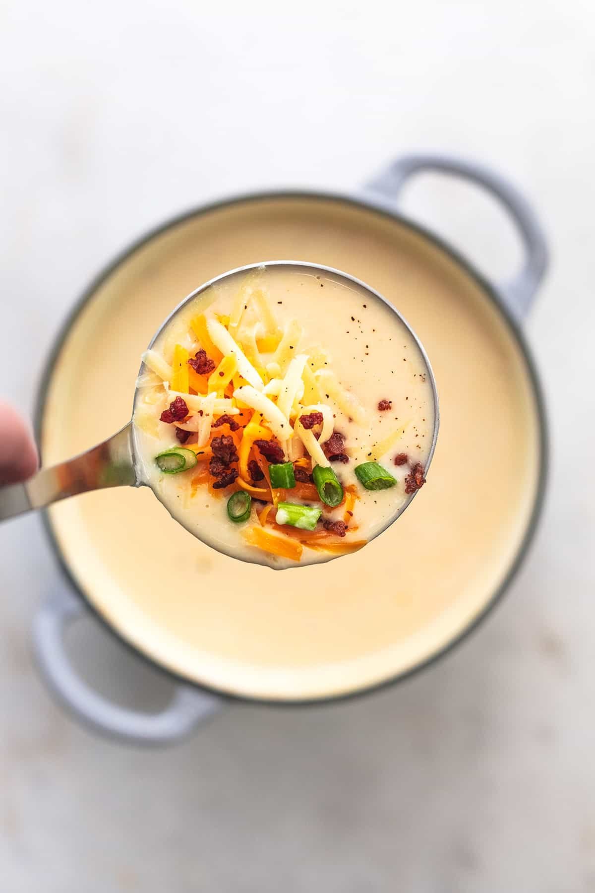 hand lifting ladle of soup above full pot of soup