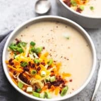 bowl of creamy potato soup with shredded cheese, bacon bits, and onions on top