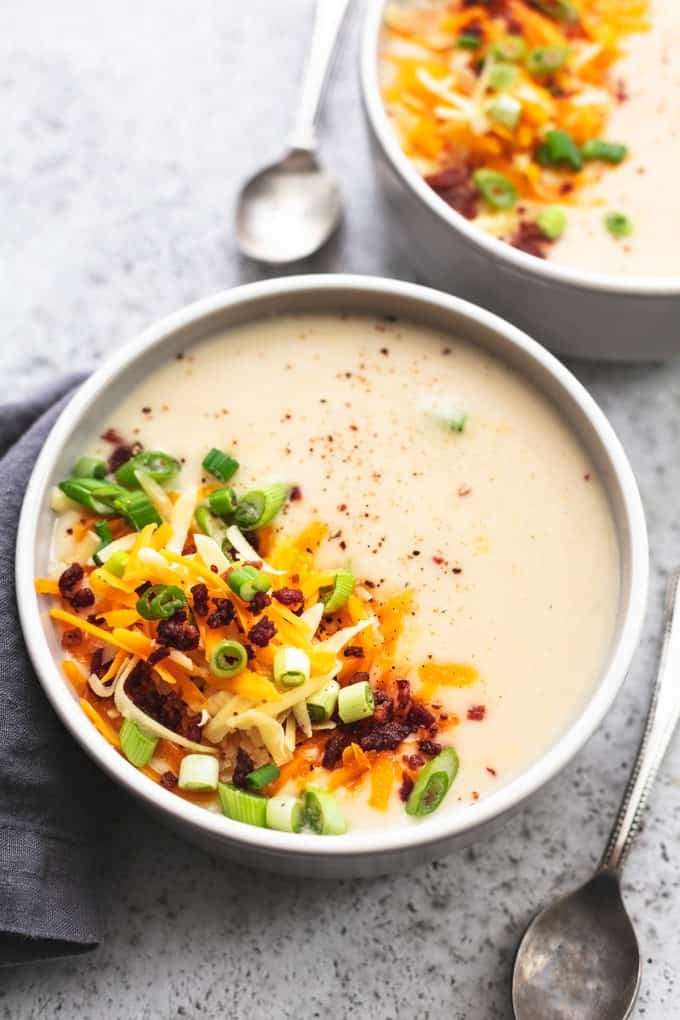 bowl of creamy potato soup with shredded cheese, bacon bits, and onions on top