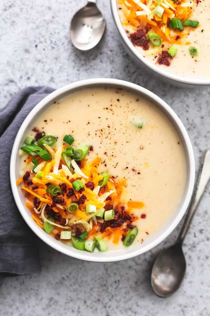soup with cheese, bacon, and green onion toppings in a bowl with a spoon