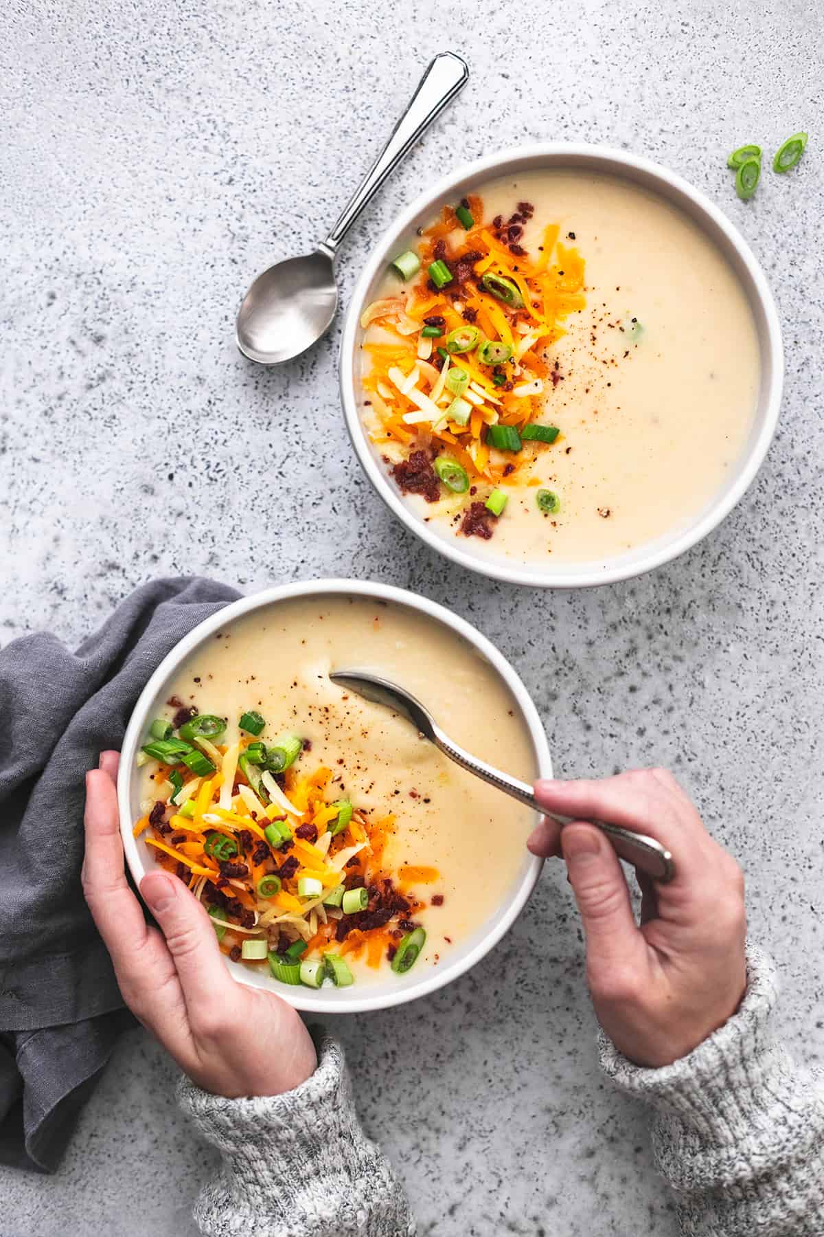 hand dipping spoon into bowl of soup with second bowl on the side