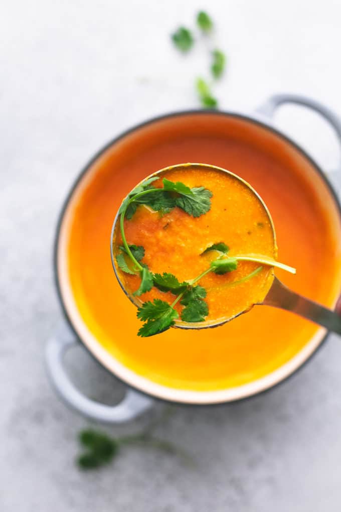 ladle of carrot soup above pot of more soup