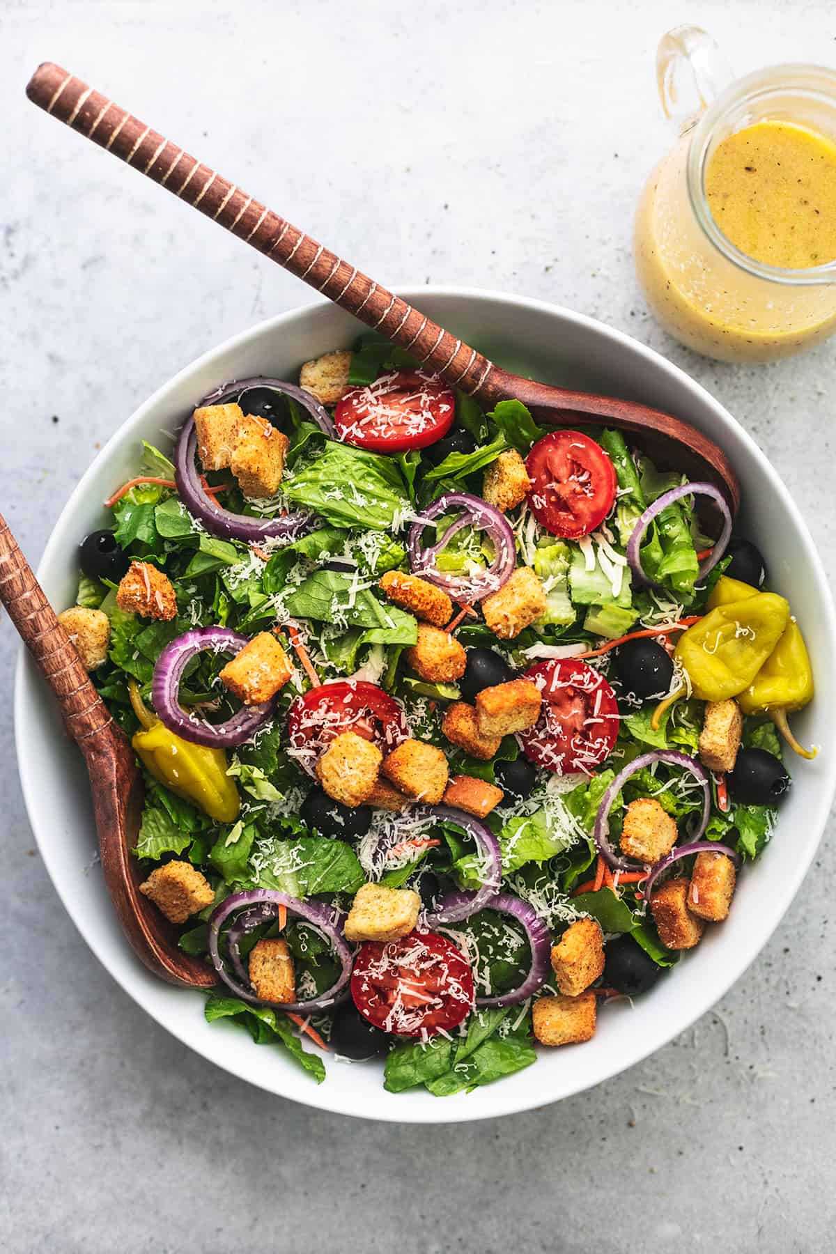 overhead view of large bowl of salad with wooden spoons and jar of dressing