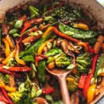 wooden serving spoon stirring vegetables in skillet