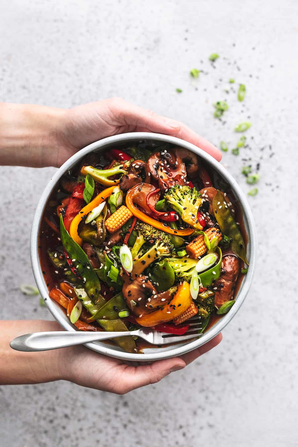 hands holding plate of stir fried vegetables