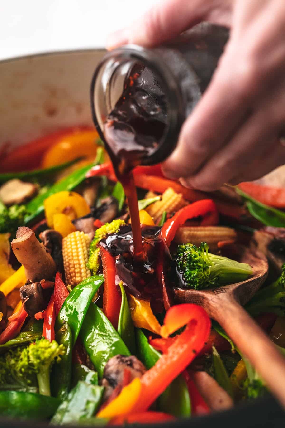 hand pouring dark sauce over vegetables in a skillet