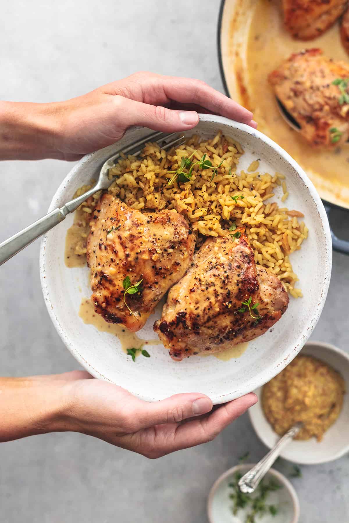 overhead view of hands holding plate of cooked chicken above skillet with more chicken