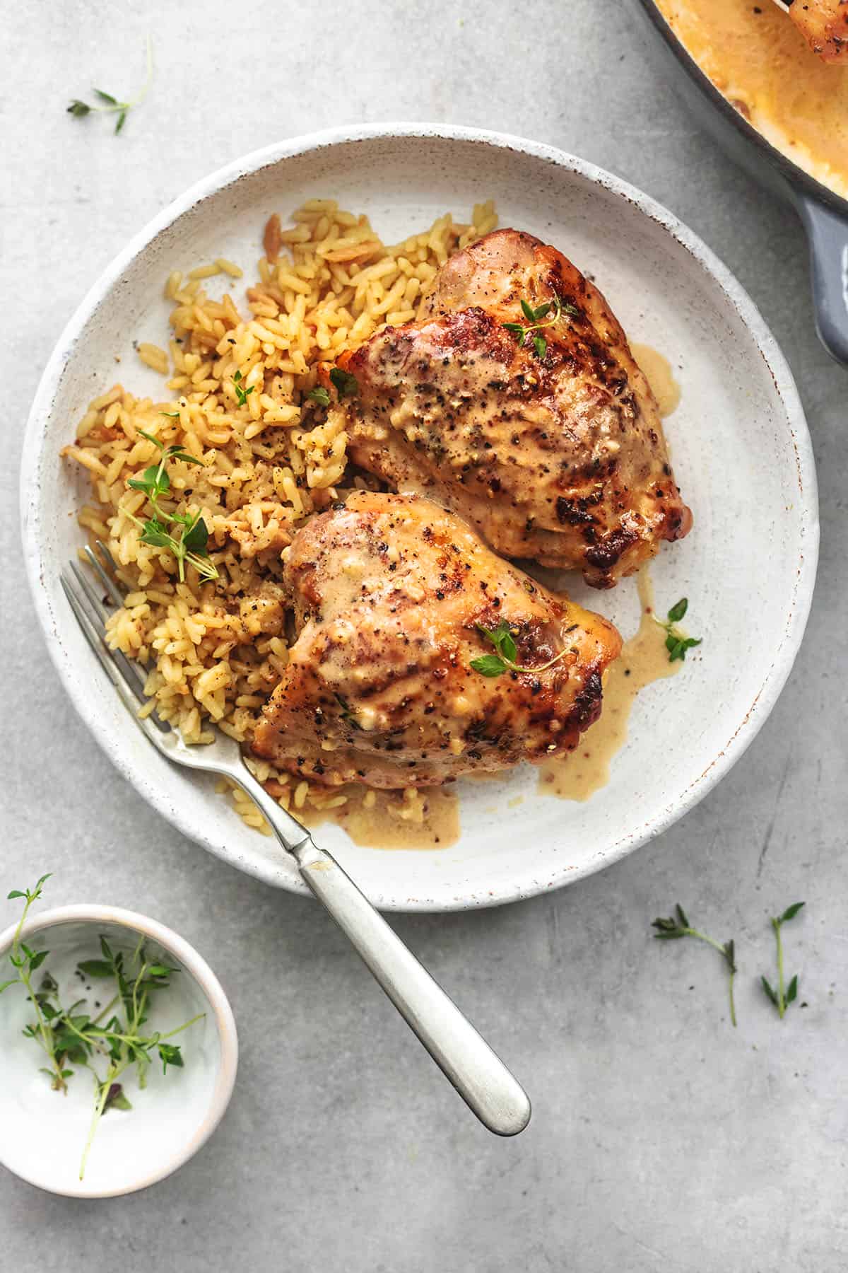 chicken thighs with sauce and rice on plate with bowl of herbs beside