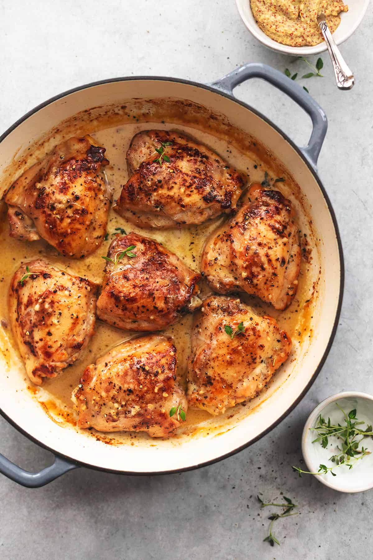 overhead view of baked chicken thighs in pan with cream sauce and herbs on the side