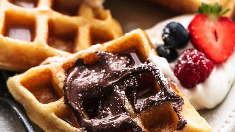 up close view of belgian waffles with nutella, powdered sugar, and fresh berries