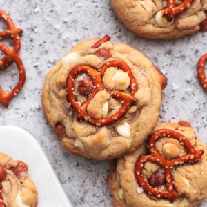 cookies layered on a table with pretzels, white chocolate chips, and caramel bits