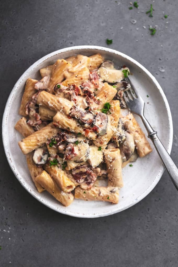 overhead view of a plate of mushroom pasta with bacon and a fork