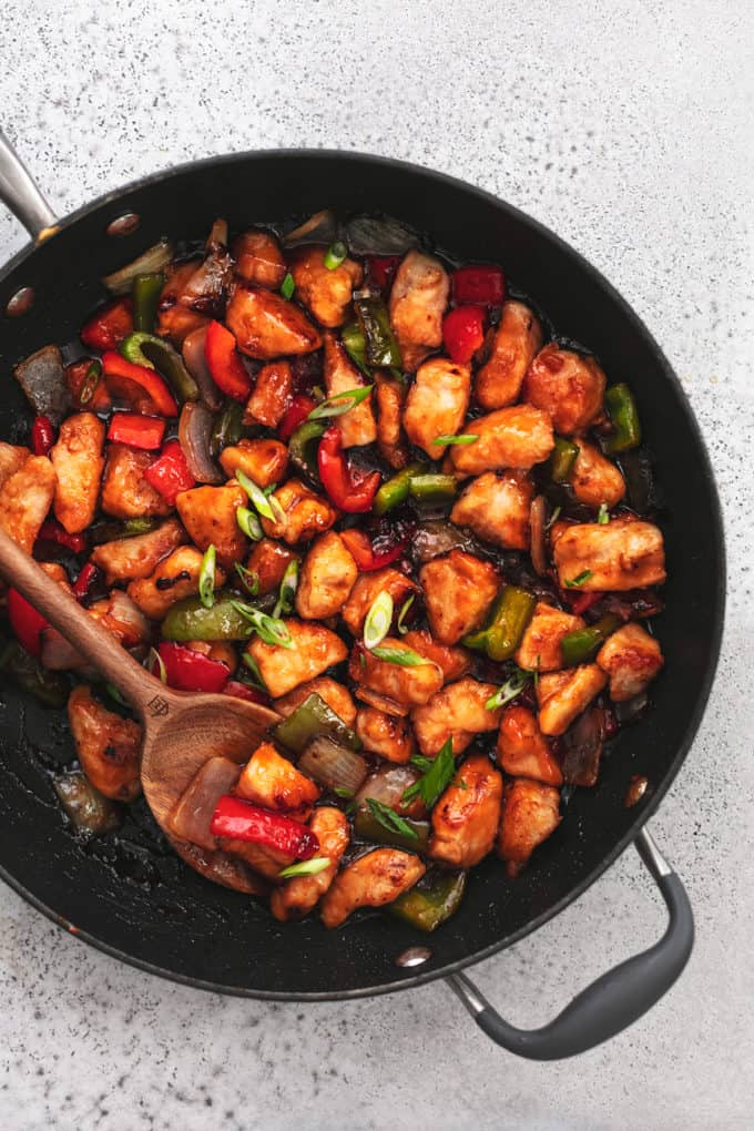 saucy chicken with bell peppers and onions cooked in a skillet with a serving spoon