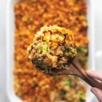 hand holding serving spoon of chicken and rice above baking dish