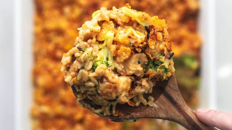 hand holding serving spoon of chicken and rice above baking dish