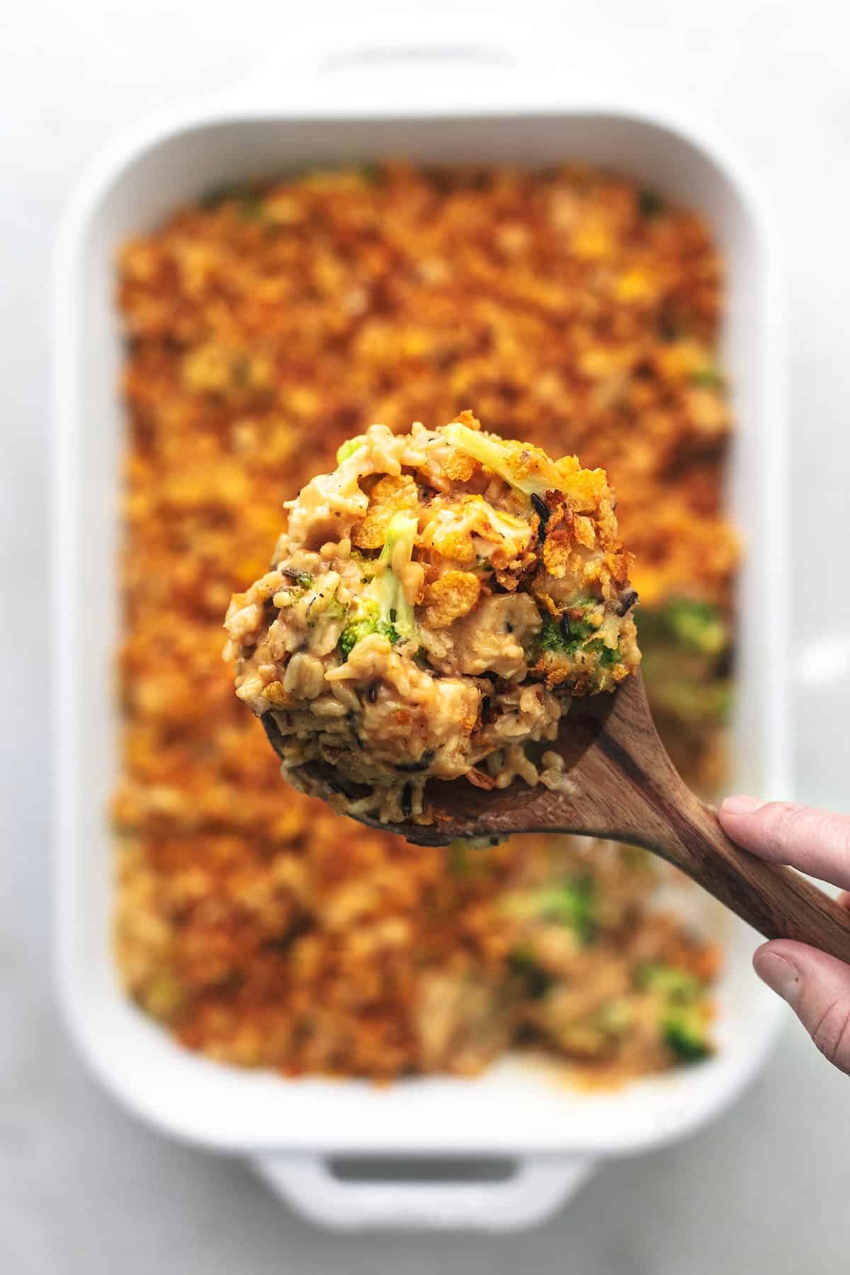 hand holding serving spoon of chicken and rice above baking dish