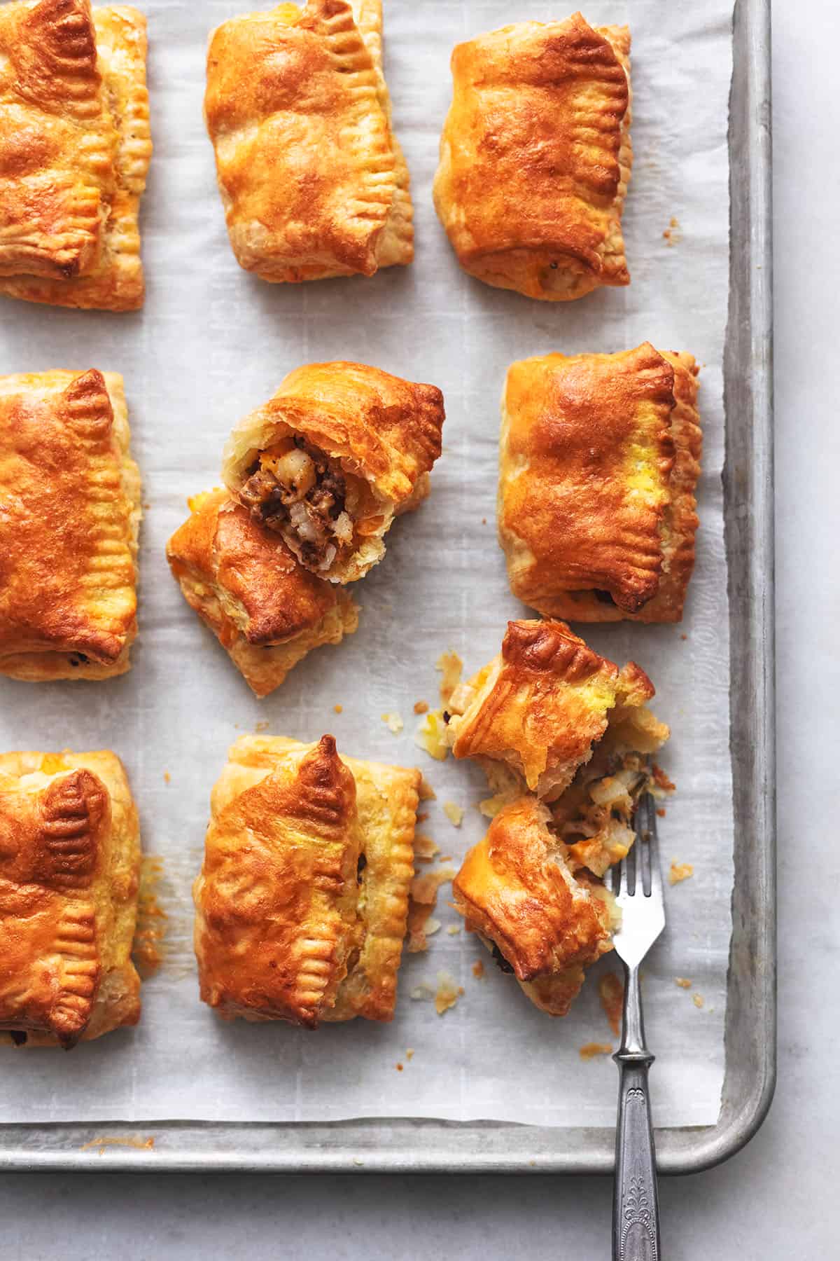 fork cutting into a puff pastry sausage roll on a sheet pan