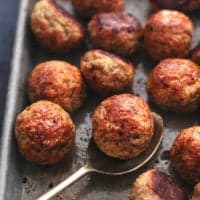 baked chicken meatballs on a sheet pan with a spoon