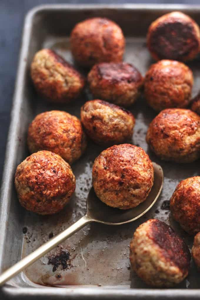 baked chicken meatballs on a sheet pan with a spoon