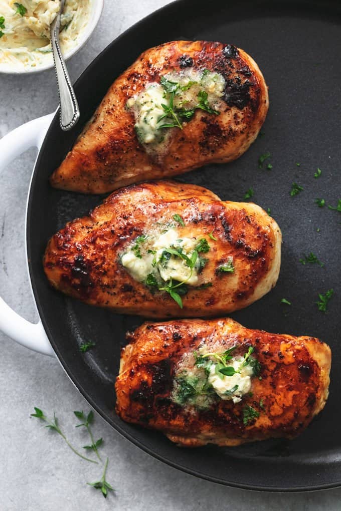 three chicken breasts on skillet topped with melting butter and herbs