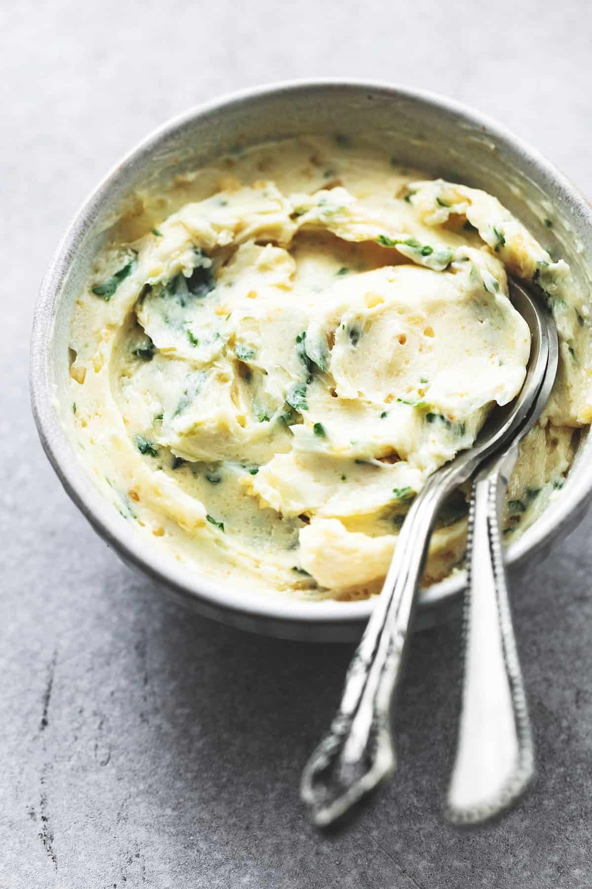 bowl of butter with garlic and herbs and two spoons