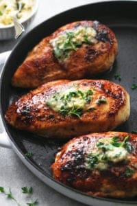 three chicken cooked chicken breasts topped with garlic butter on a skillet