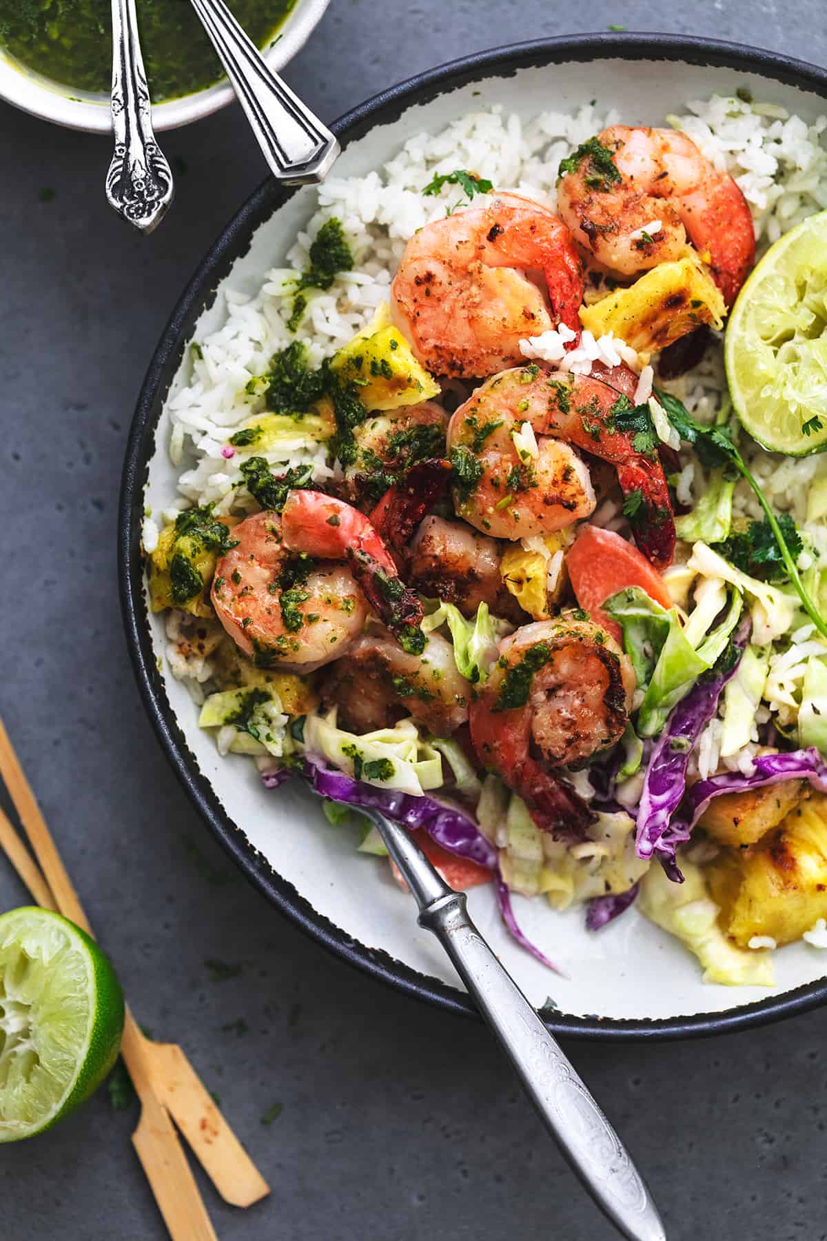 fork digging into bowl of shrimp and rice with lime wedges and slaw