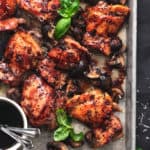 sheet pan with baked chicken thighs and fresh basil leaves