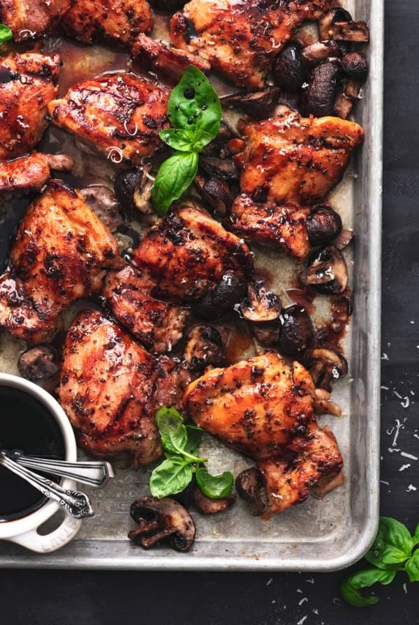 sheet pan with baked chicken thighs and fresh basil leaves