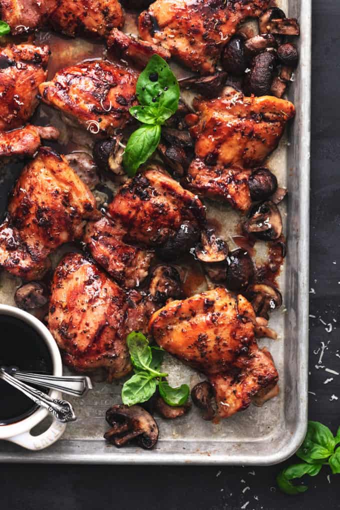 sheet pan with baked chicken thighs and fresh basil leaves