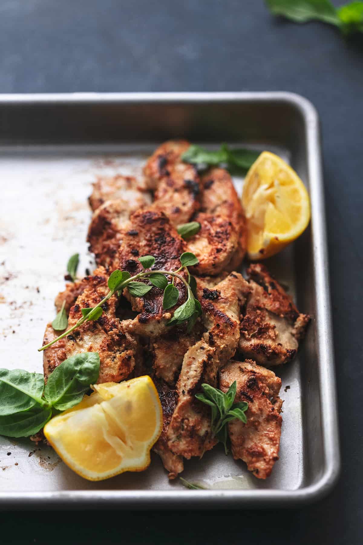 cooked chicken strips with herbs and lemon wedges on baking pan