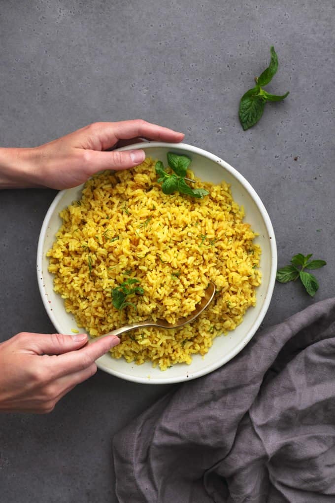 hands scooping spoon into bowl of lemon rice