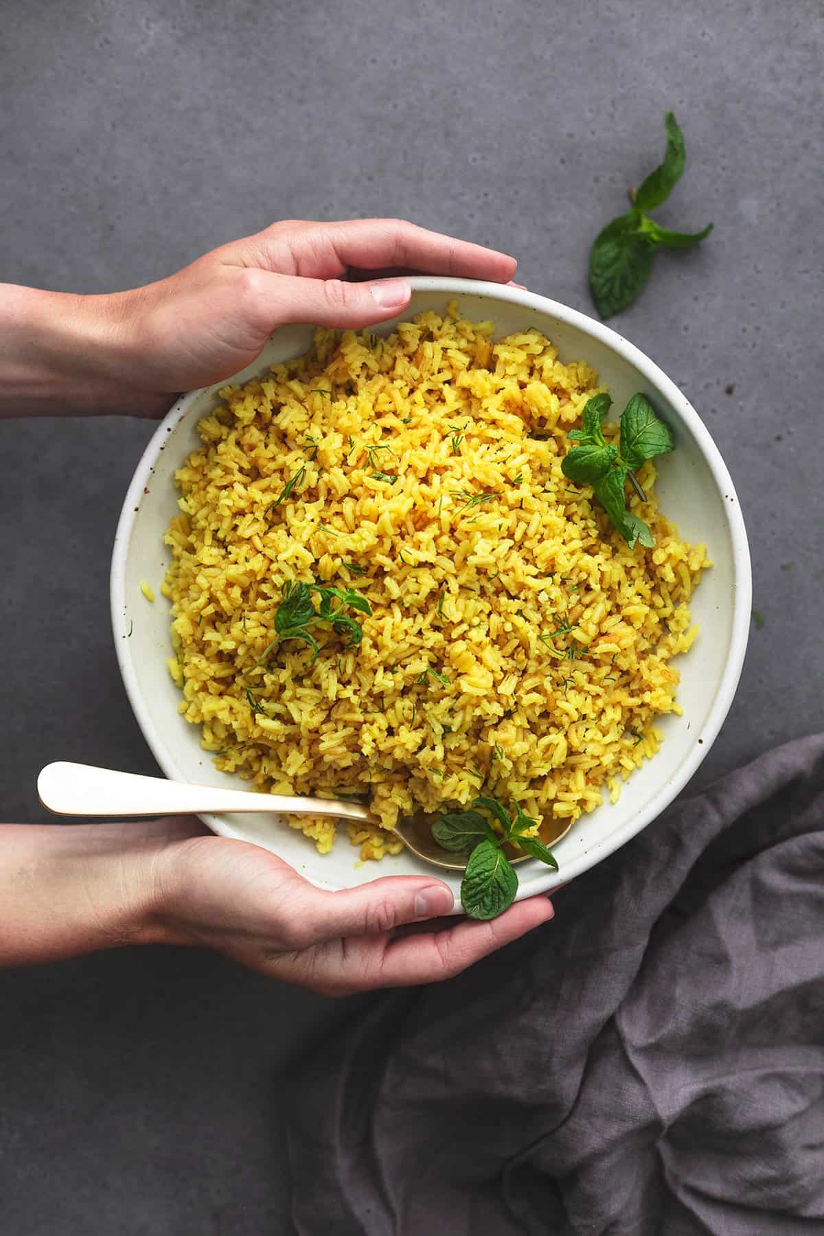 hands holding platter of rice with a few mint leaves and serving spoon