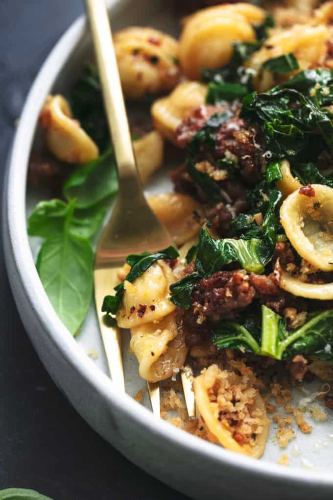 fork scopping up pasta noodles with greens and meat