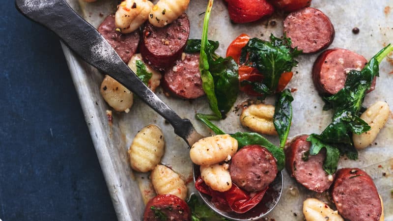 sheet pan with serving spoon scooping sausage and gnocchi
