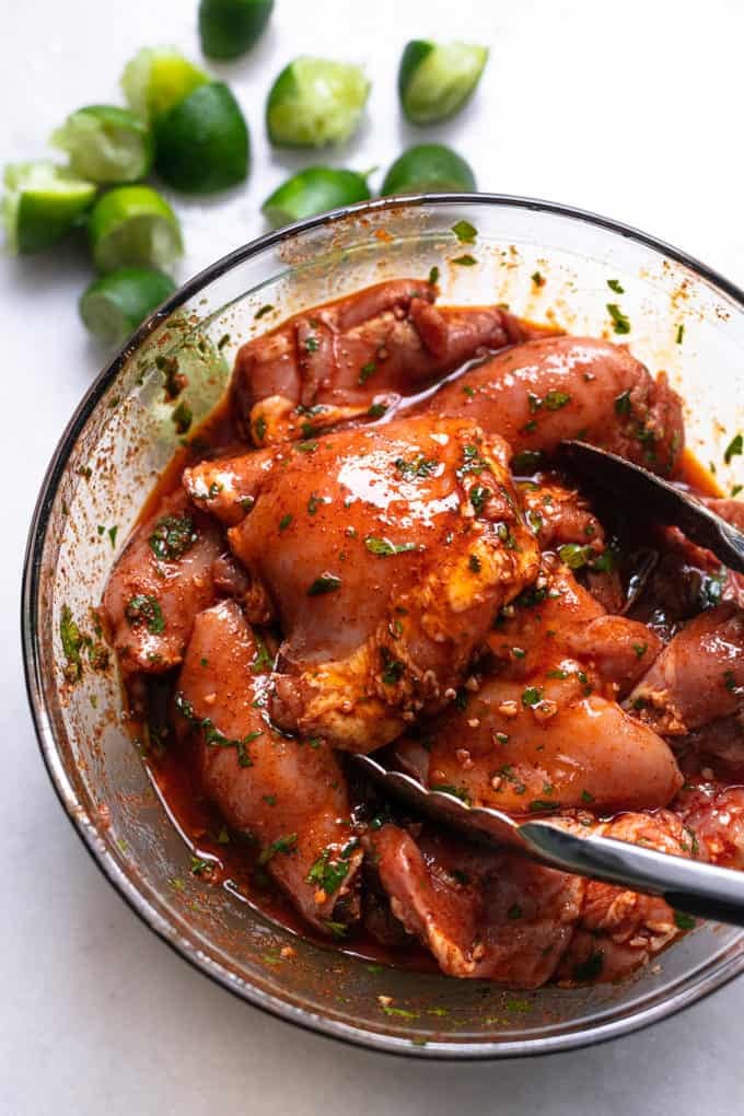 chicken thighs marinating in bowl of sauce with tongs