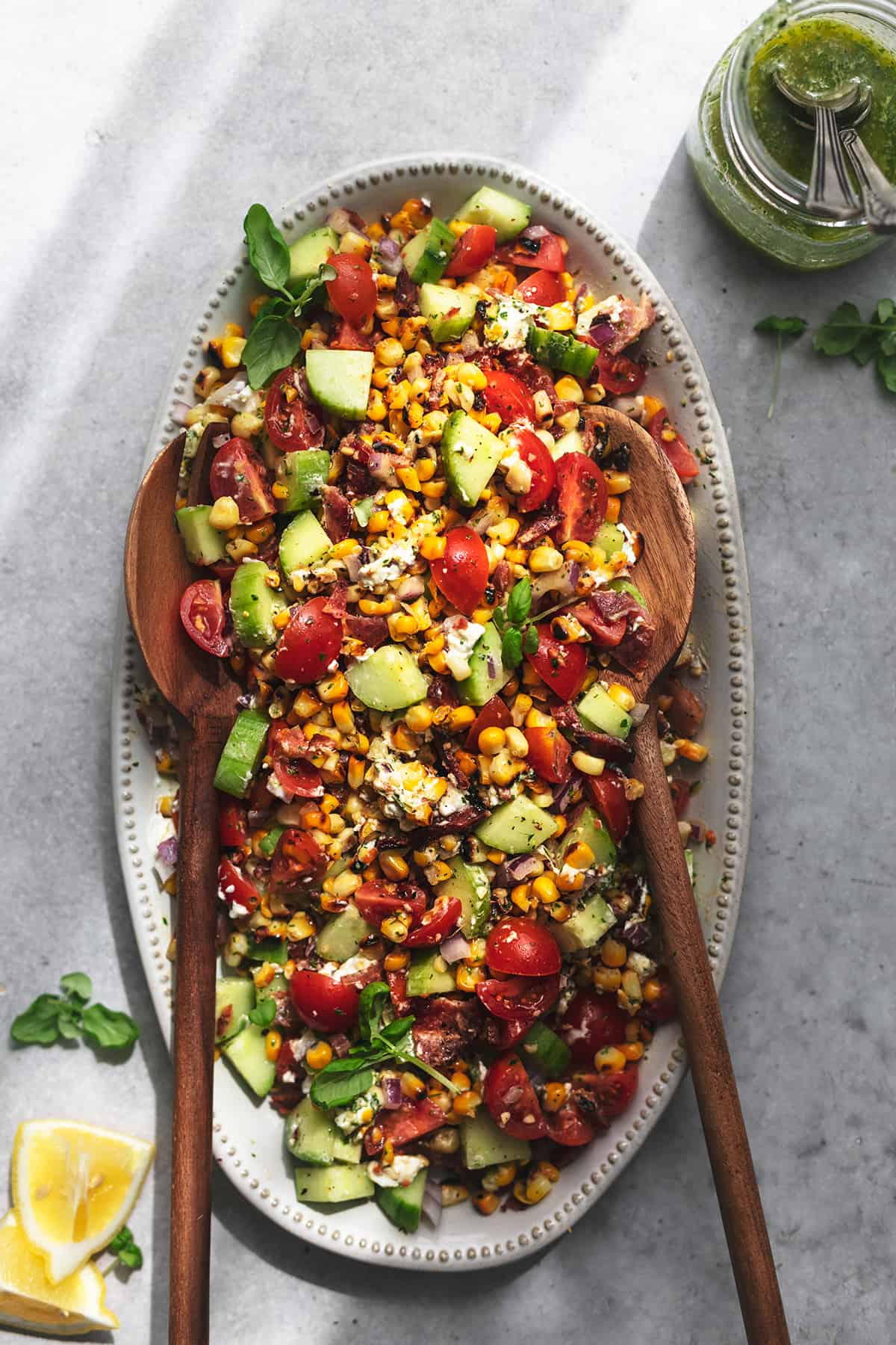 platter of corn salad with lemon wedges and herb dressing in a jar