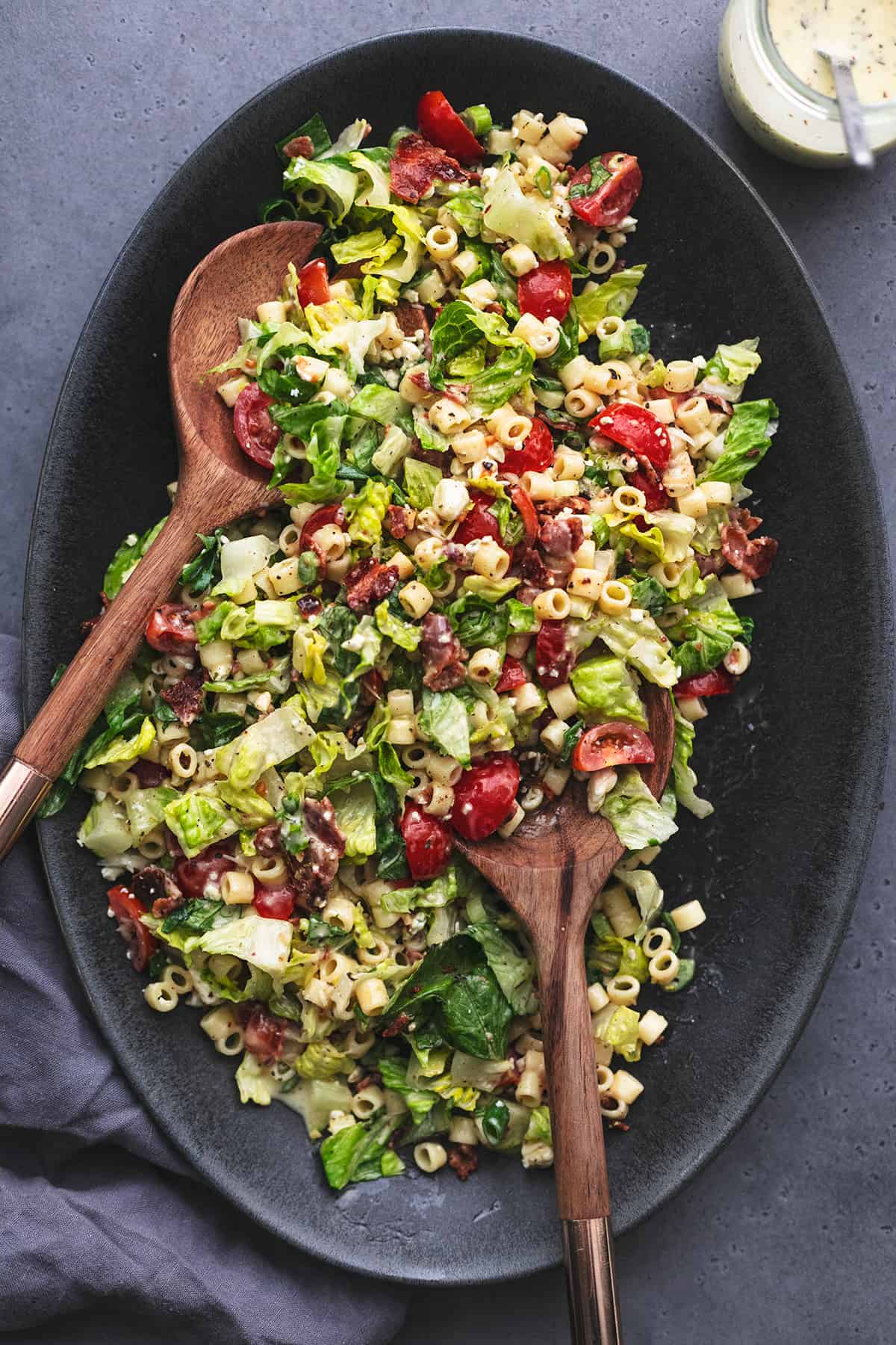 wooden salad spoons tossing chopped salad with pasta ditalini noodles and tomatoes and bacon