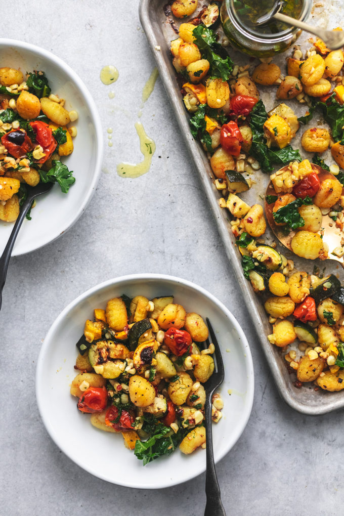 two bowls of roasted gnocchi with vegetables and part of a sheet pan with more