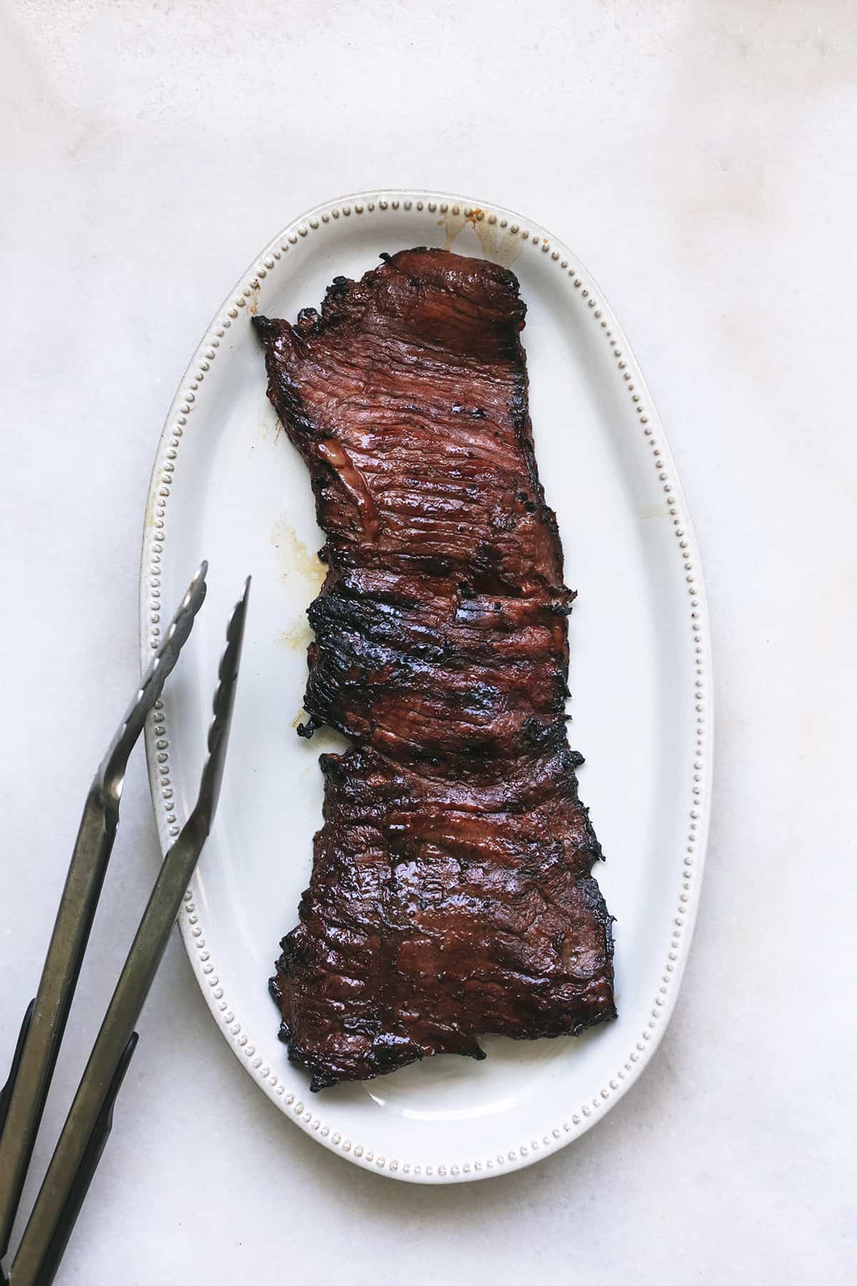 marinated and grilled skirt steak with tongs on a platter