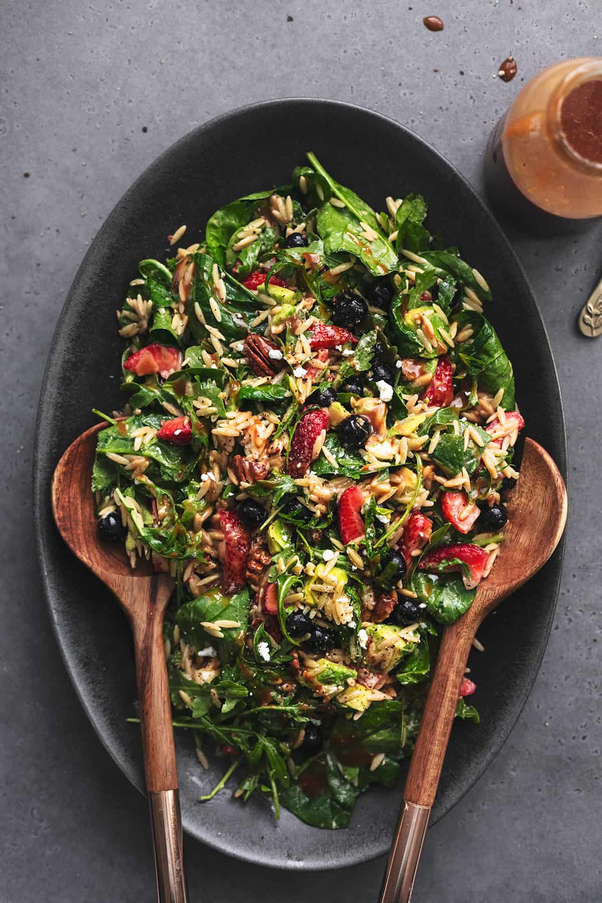 serving platter with spinach and berry salad with serving spoons and jar of dressing