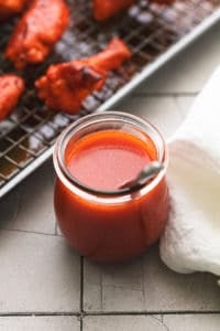 jar of buffalo sauce with spoon beside napkin and baking sheet of wings