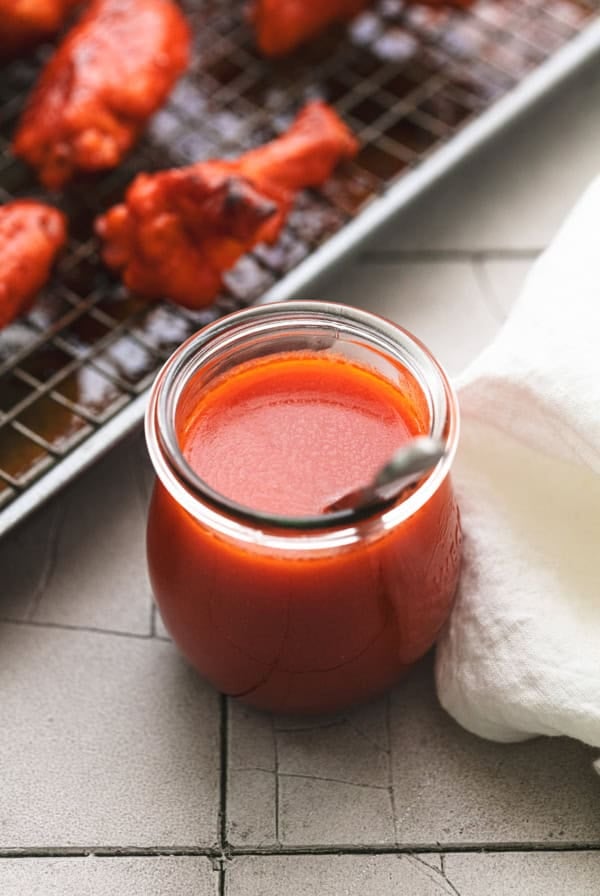 jar of buffalo sauce with spoon beside napkin and baking sheet of wings