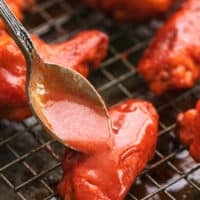 spoon pouring buffalo sauce onto chicken wings on a baking rack