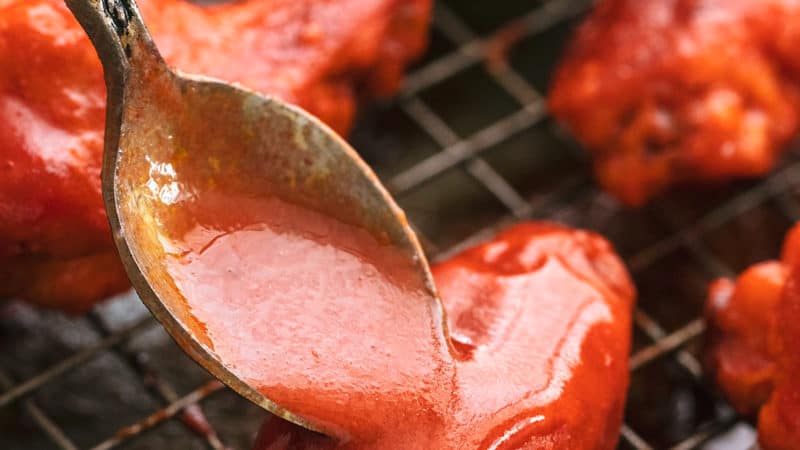 spoon pouring buffalo sauce onto chicken wings on a baking rack