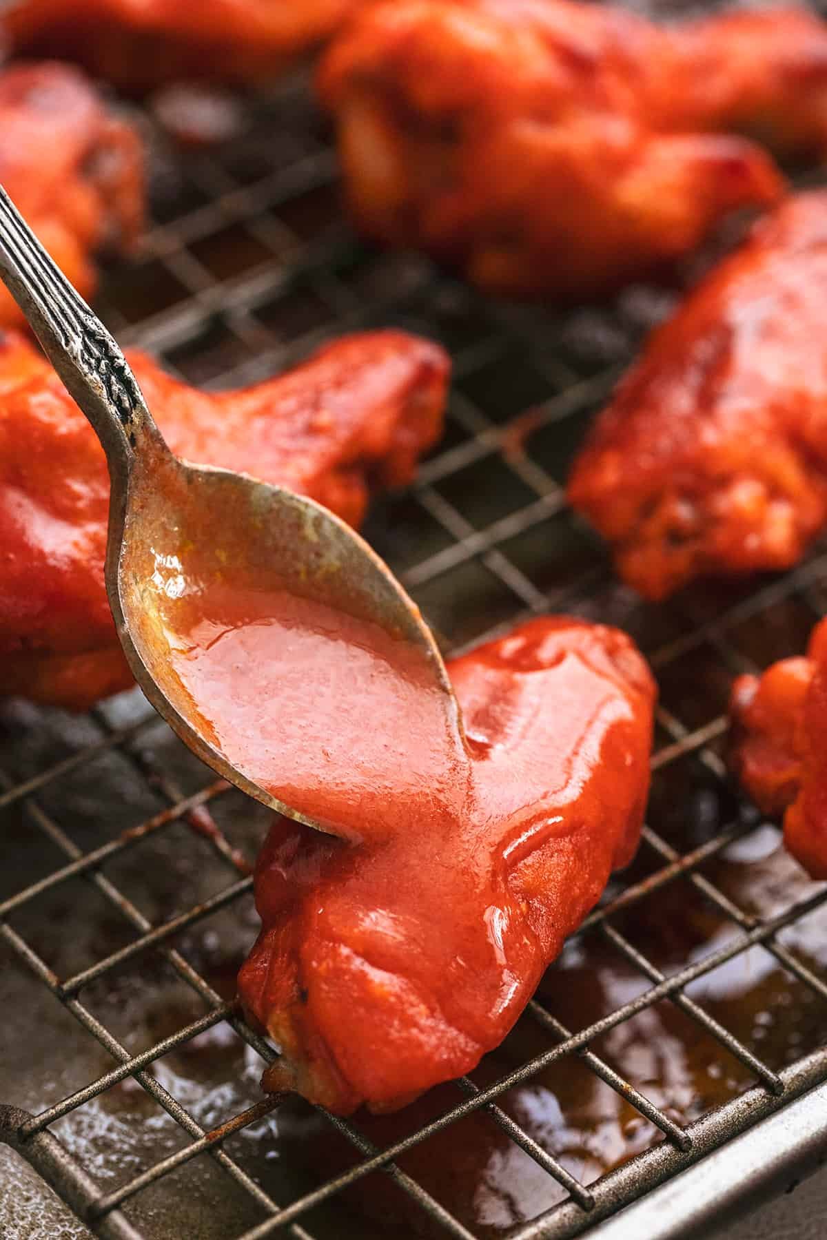 spoon pouring buffalo sauce onto chicken wings on a baking rack