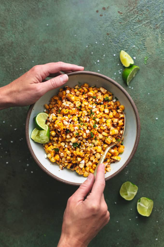 hands holding bowl of corn salad with lime wedges