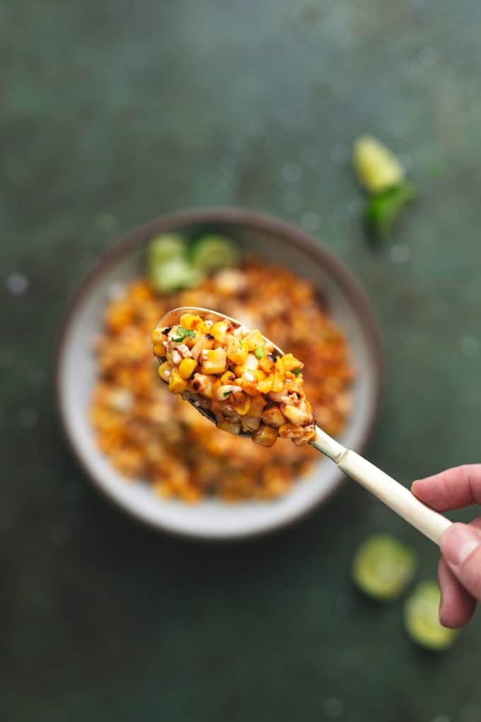 hand holding single spoon of corn above a bowl