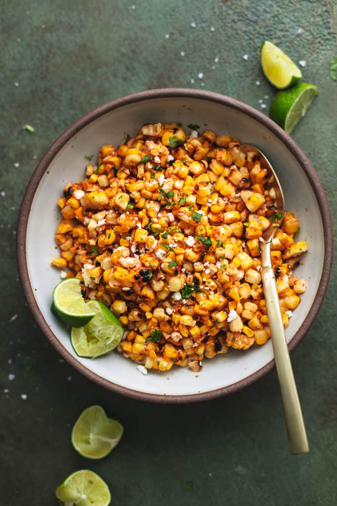 mexican street corn salad with spoon and lime wedges in bowl