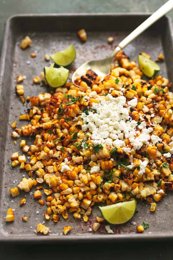 pile of corn, cilantro, lime wedges, cotija cheese on sheet pan